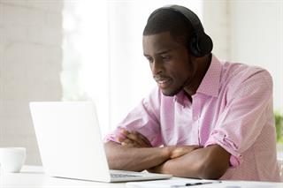 Man wearing headset seated and listening while looking at laptop screen